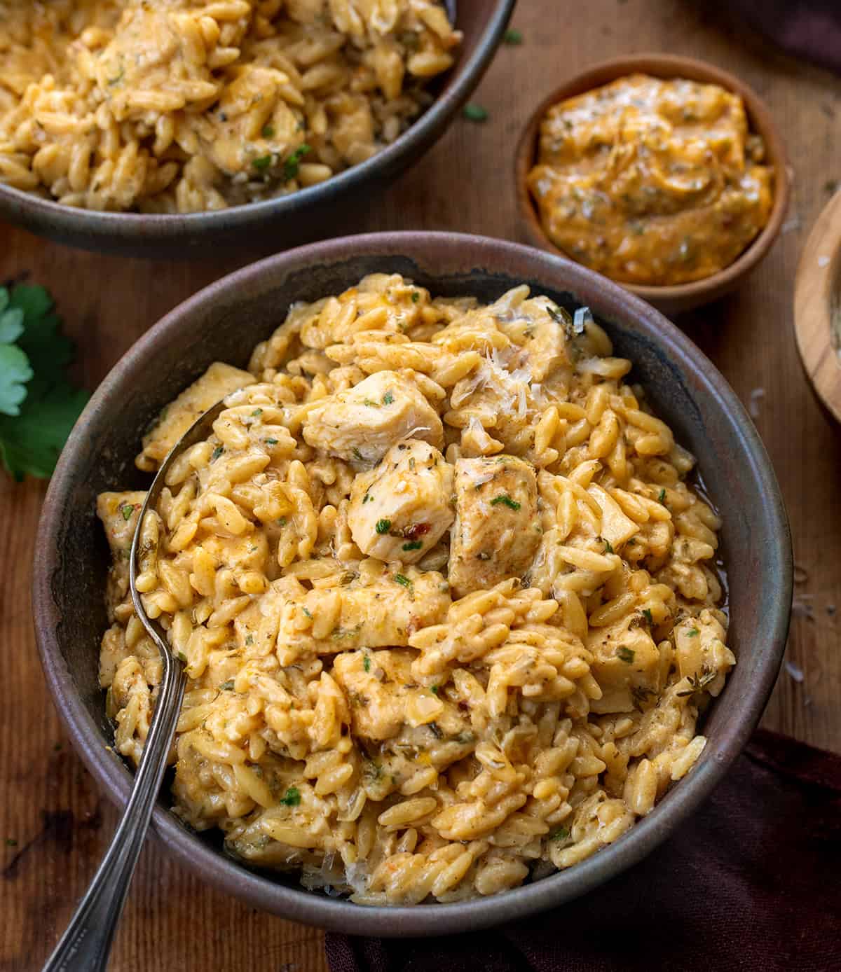Bowls of Cowboy Butter Chicken Orzo on a wooden table with a ramekin of cowboy butter Bowls of Cowboy Butter Chicken Orzo on a wooden table with a ramekin of cowboy butter.