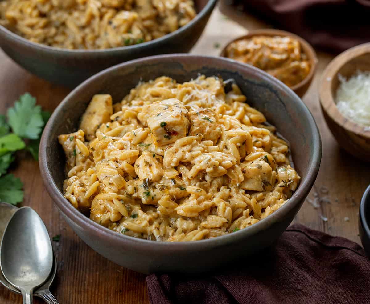 Bowls of Cowboy Butter Chicken Orzo on a wooden table with a ramekin of cowboy butter Bowls of Cowboy Butter Chicken Orzo on a wooden table with a ramekin of cowboy butter.