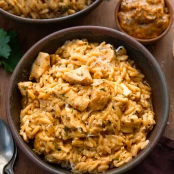 Bowls of Cowboy Butter Chicken Orzo on a wooden table with a ramekin of cowboy butter.