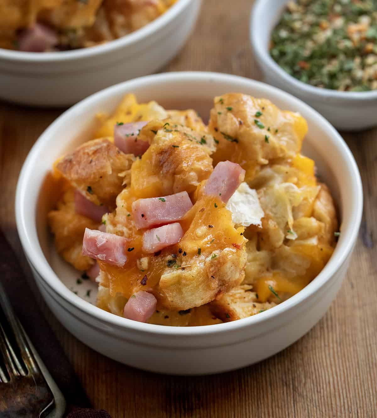 Bowls of Cowboy Butter Ham and Cheese Croissant Bake on a wooden table with Cowboy Seasoning.