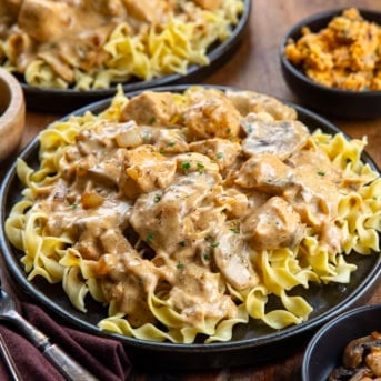 Plates of Cowboy Chicken Stroganoff on a wooden table next to cowboy butter.
