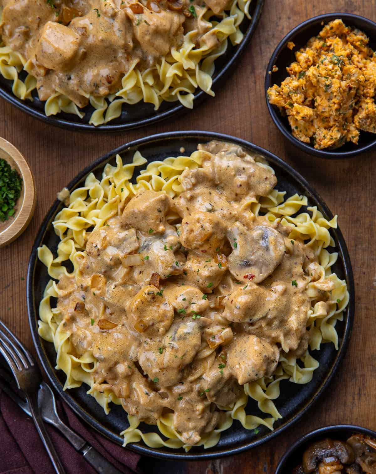 Plates of Cowboy Chicken Stroganoff on a wooden table with cowboy butter from overhead Plates of Cowboy Chicken Stroganoff on a wooden table with cowboy butter from overhead.