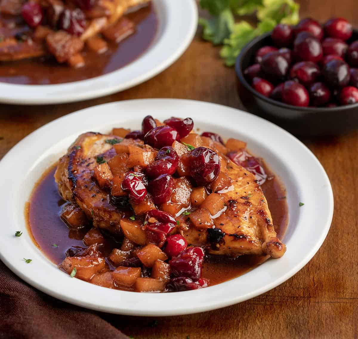 White plates with Cranberry Apple Chicken on them on a wooden table White plates with Cranberry Apple Chicken on them on a wooden table.
