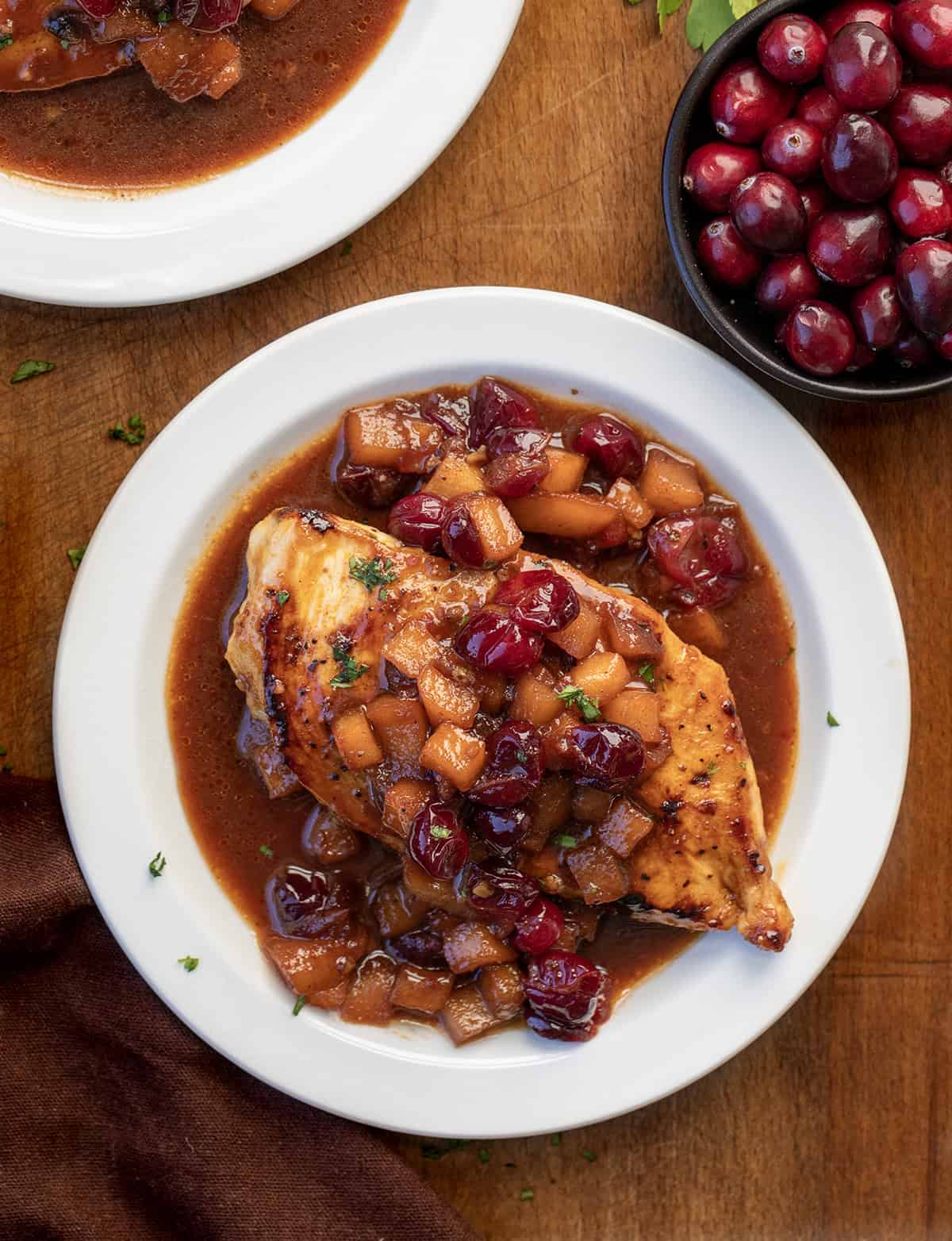 White plates with Cranberry Apple Chicken on them on a wooden table White plates with Cranberry Apple Chicken on them on a wooden table.