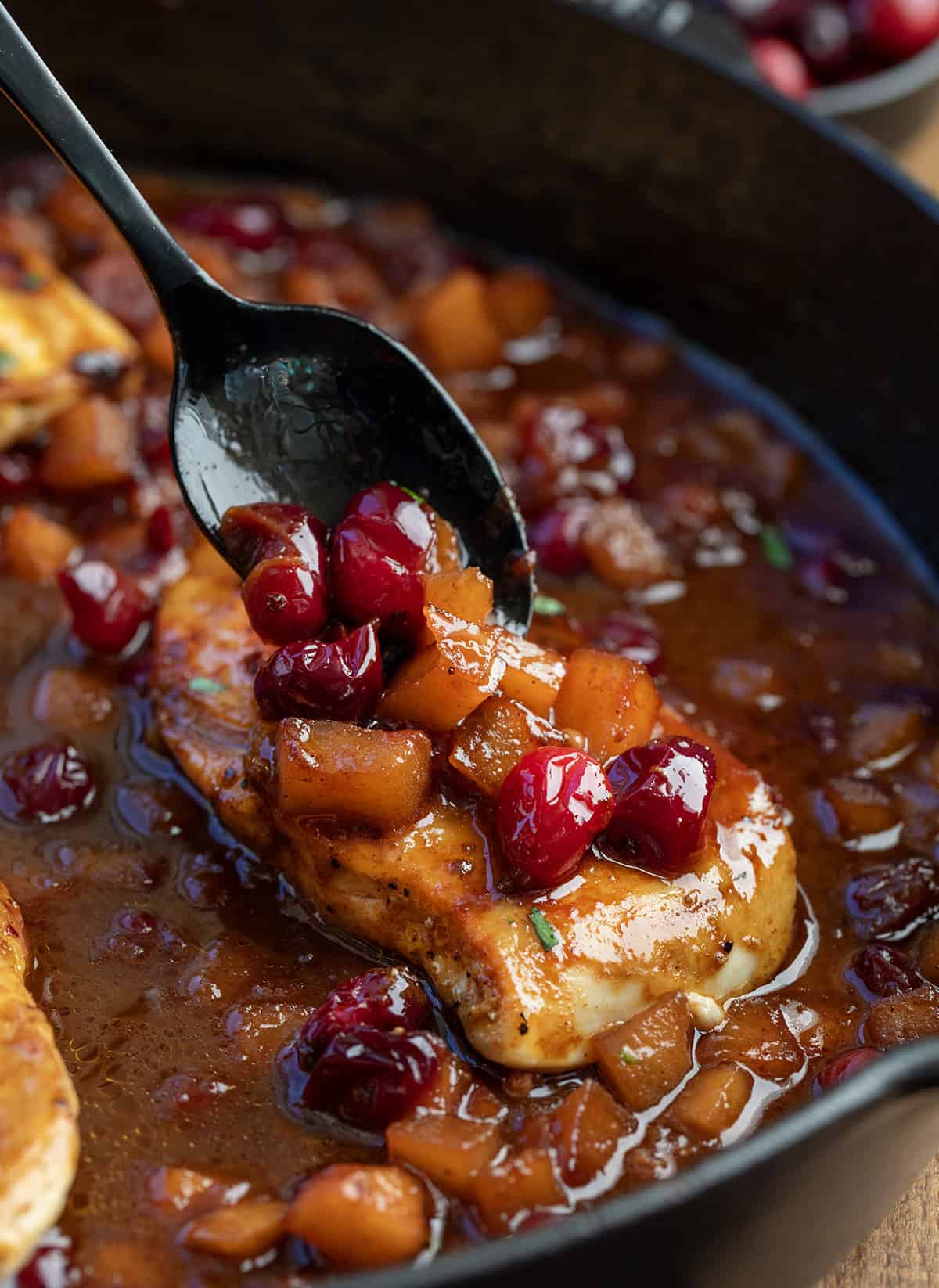 Spooning cranberry apple sauce over Chicken in a skillet Spooning cranberry apple sauce over Chicken in a skillet.