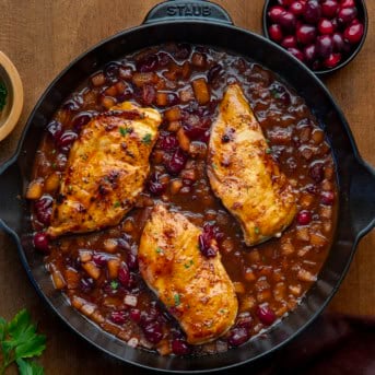 Cranberry Apple Chicken in a skillet on a wooden table from overhead.
