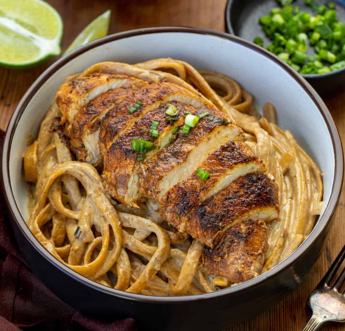 Bowl of Jerk Chicken Alfredo Pasta on a wooden table Bowl of Jerk Chicken Alfredo Pasta on a wooden table.