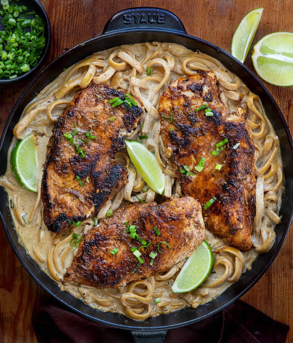 Jerk Chicken Alfredo in a skillet on a wooden table from overhead Jerk Chicken Alfredo in a skillet on a wooden table from overhead.