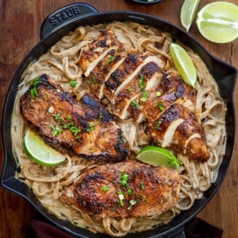 Jerk Chicken Alfredo in a skillet on a wooden table with one piece of chicken cut into slices.