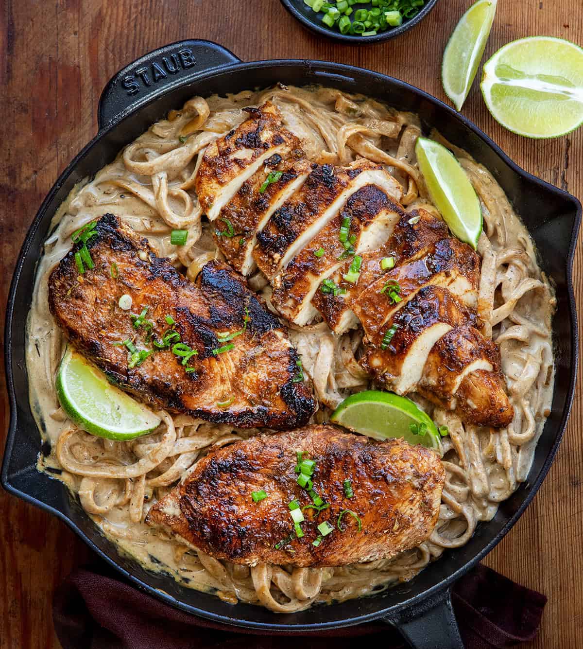 Jerk Chicken Alfredo in a skillet on a wooden table with one piece of chicken cut into slices Jerk Chicken Alfredo in a skillet on a wooden table with one piece of chicken cut into slices.