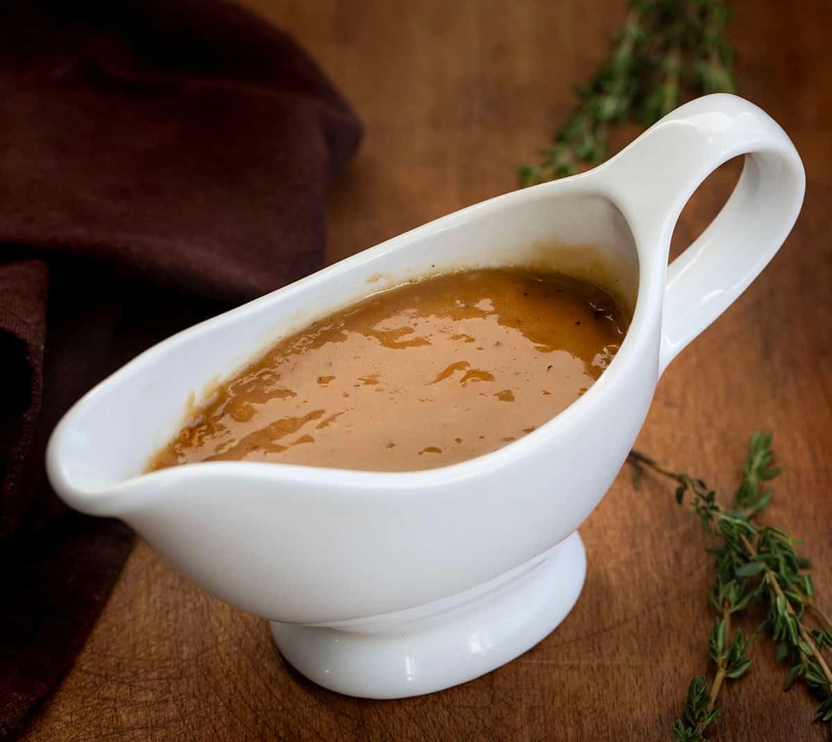 Gravy boat filled with Make-Ahead Turkey Gravy on a wooden table Gravy boat filled with Make-Ahead Turkey Gravy on a wooden table.