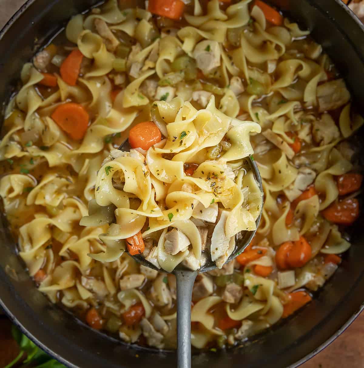 Ladle full of Roasted Garlic Chicken Noodle Soup being held above the pot Ladle full of Roasted Garlic Chicken Noodle Soup being held above the pot.