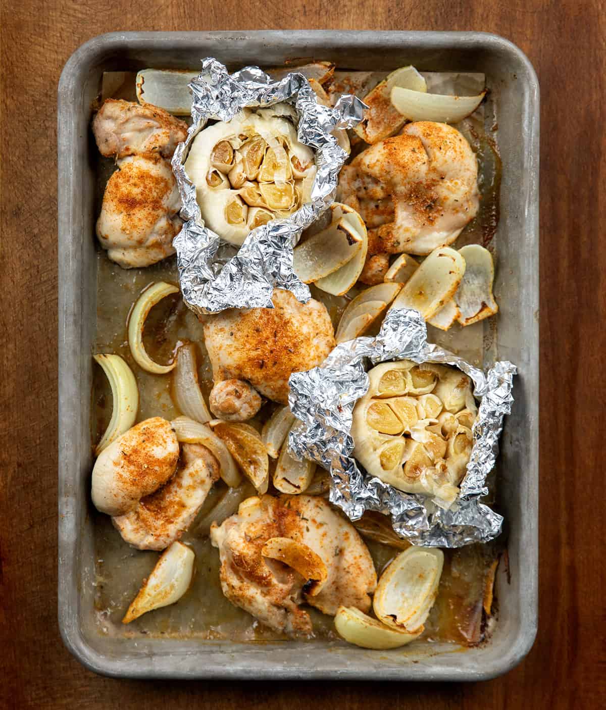 Sheet pan of roasted garlic, chicken, and onions on a wooden table from overhead Sheet pan of roasted garlic, chicken, and onions on a wooden table from overhead.