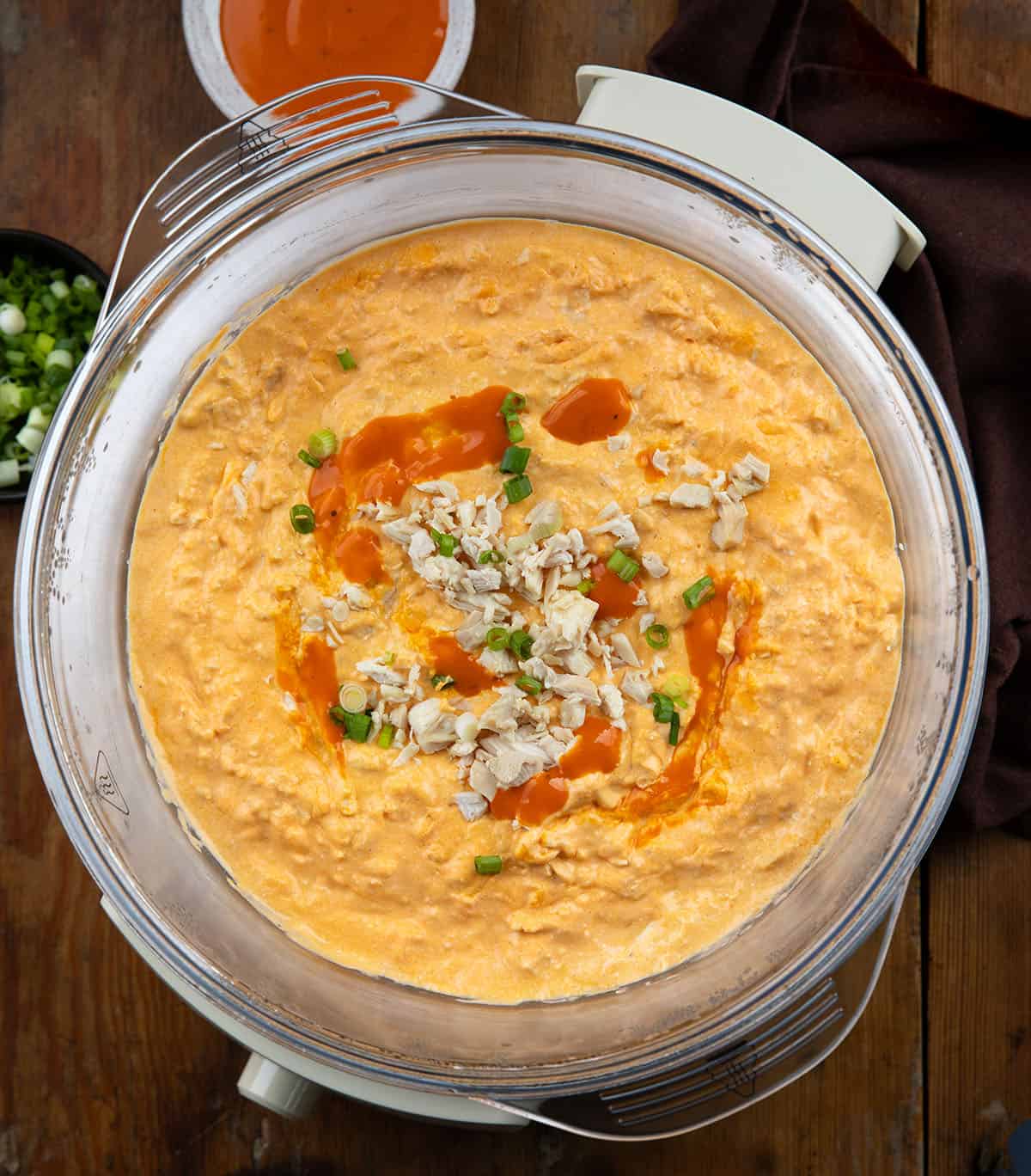 Slow Cooker Buffalo Chicken Dip on a wooden table from overhead Slow Cooker Buffalo Chicken Dip on a wooden table from overhead.