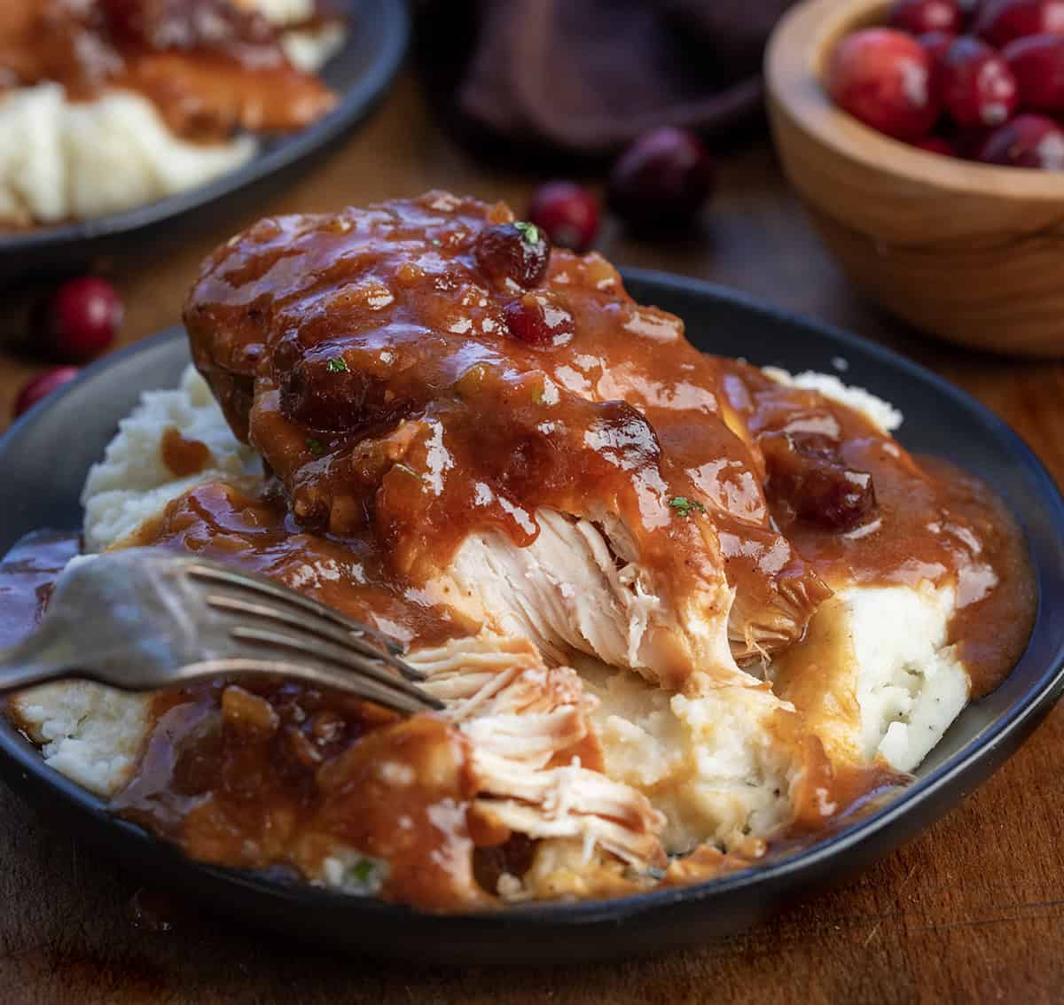 Fork shredding Slow Cooker Cranberry Chicken on a plate of mashed potatoes.