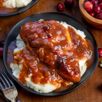 Black plates of Slow Cooker Cranberry Chicken on mashed potatoes.