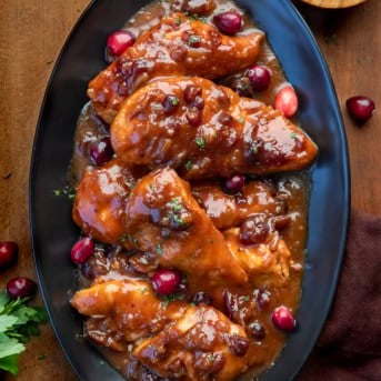 Black platter of Slow Cooker Cranberry Chicken on a wooden table from overhead.