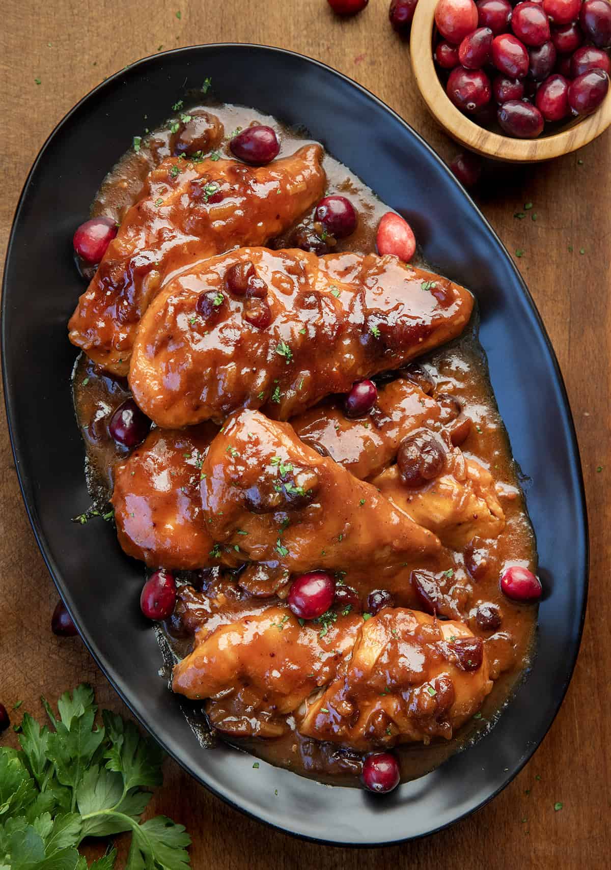 Black platter of Slow Cooker Cranberry Chicken on a wooden table from overhead.