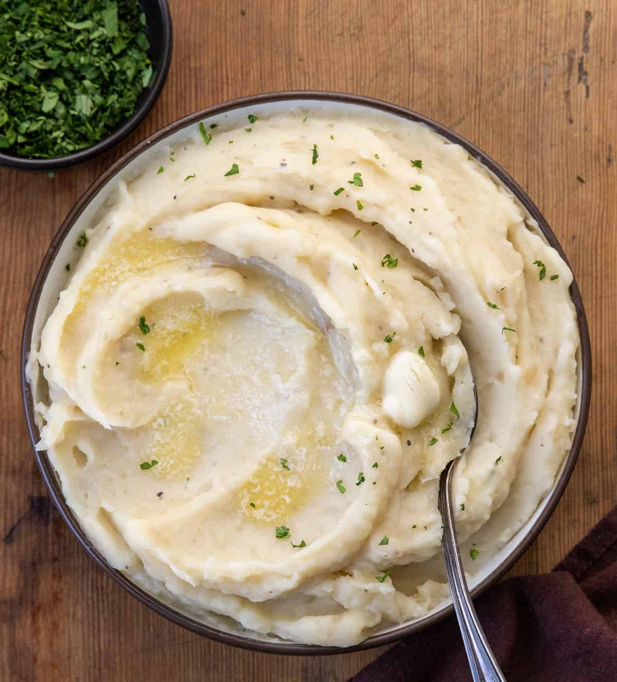 Bowl of Slow Cooker Mashed Potatoes on a wooden table and with a spoon in it Bowl of Slow Cooker Mashed Potatoes on a wooden table and with a spoon in it.